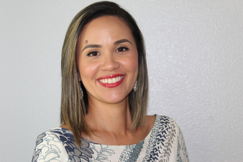 Smiling photo of Daphne Tong-Pave, Director of Compliance at Nakupuna Companies, with black hair and blond highlights. She is wearing earrings and a blue white blouse.