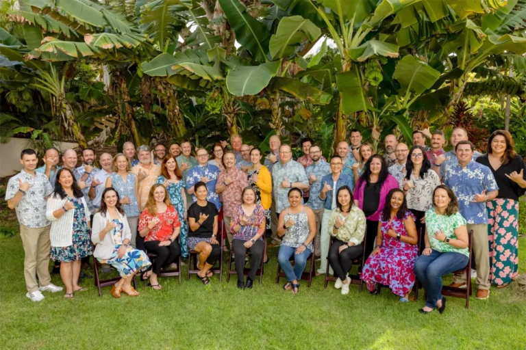 Senior Leadership Team A diverse group of Nakupuna Companies executives and management at the 2024 Senior Leadership offsite, many in Hawaiian shirts, pose for a group photo in a lush tropical garden.