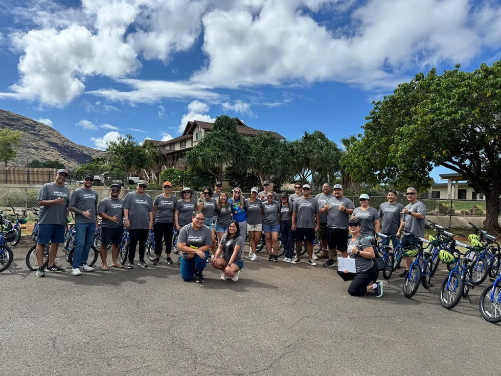 Wish For Wheels Project Kupu Nakupuna Companies Nakupuna employees volunteer with Wish for Wheels Hawai'i, building bikes for kids. This photo shows Hawaii's Most Charitable Companies award winner with a group of volunteers and completed bicycles under a partly cloudy sky. This image is featured on the Nakupuna Companies website.