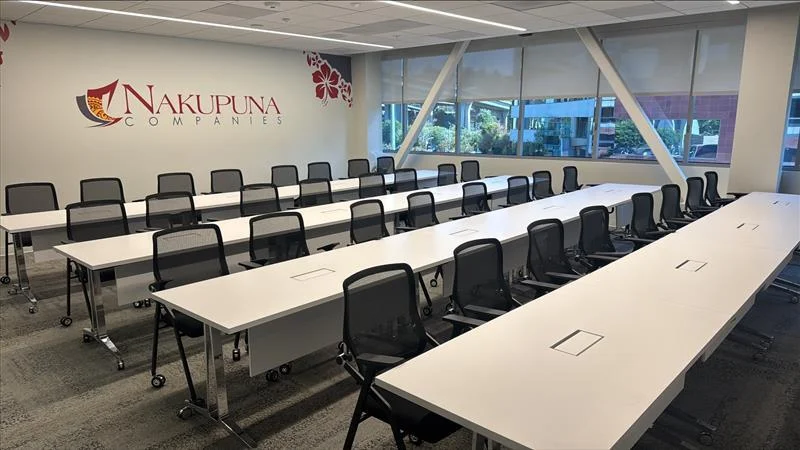 Nakupuna Companies - San Diego Interior 3 Nakupuna Companies San Diego office features a modern conference room with rows of white tables and black chairs, overlooking a bright, sunlit exterior. The Nakupuna logo is visible on the wall, celebrating Nakupuna West Coast expansion.